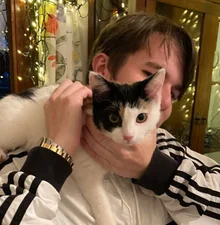 Paul holding a black and white cat up to his face, fairy lights behind